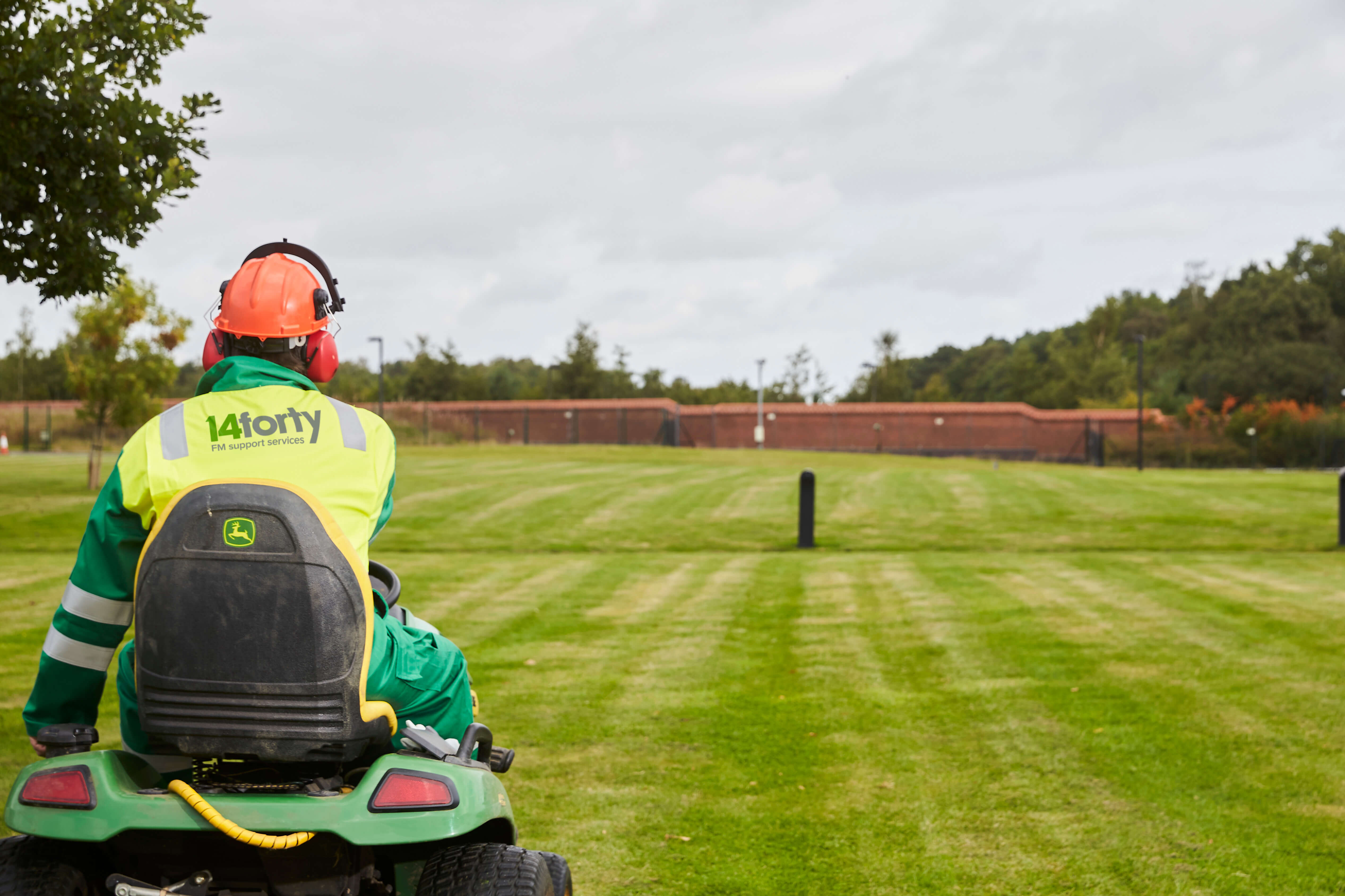 A member of 14forty's outdoor maintenance staff wearing branded fluorescent safety clothing riding a sit-on lawn mower on a large freshly cut lawn.